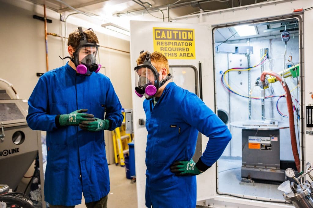 Two men suited up in the Cold Spray lab talking