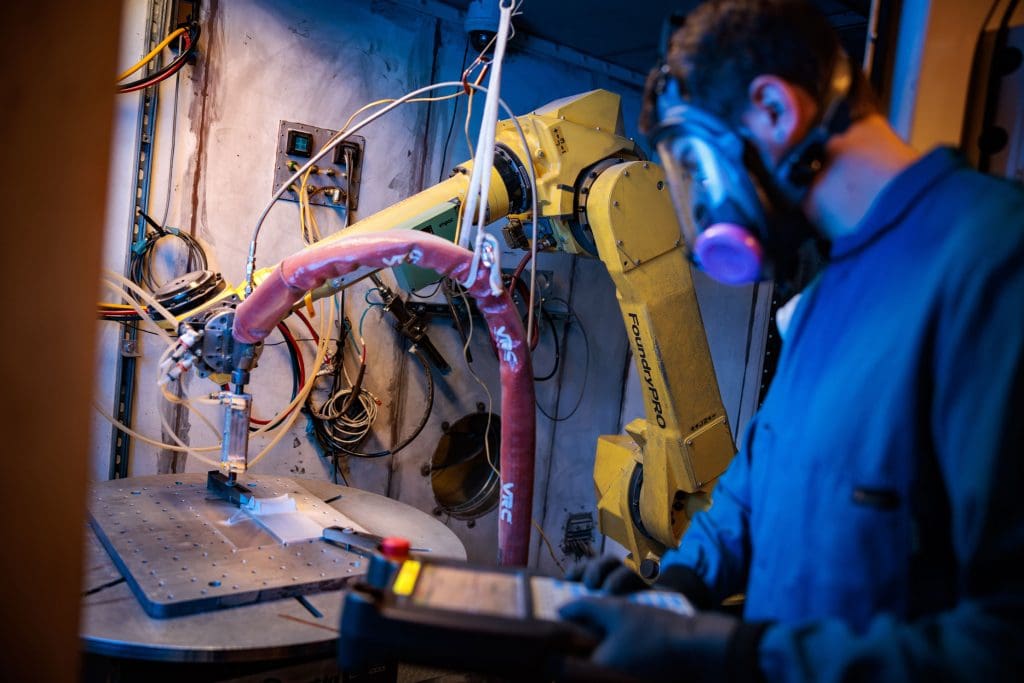 A man suited up looking at machinery in the Cold Spray lab